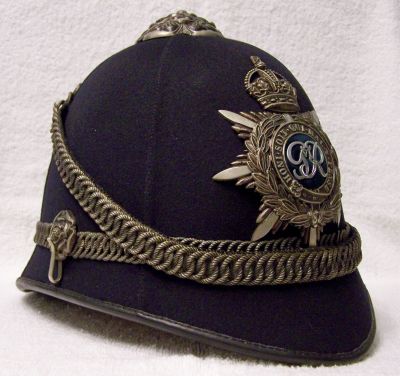 Metropolitan Chief Superintendents Ceremonial Helmet, 1938 - 1954
Metropolitan Chief Superintendents Ceremonial Helmet '1938 - 1954'. Very high quality helmet manufactured by Compton & Webb. Gunmetal coloured fittings comprising rosetop, multi piece helmet plate, roped chained centre band, twin ear rosettes supporting a roped chinchain to match the centre band, hooked up at the rear. Leather and silk lining. 
Keywords: metropolitan helmet Headwear