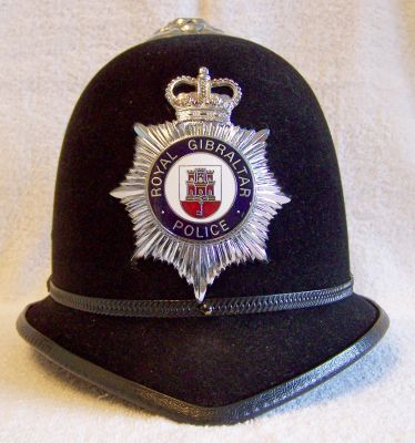 Royal Gibralter Police
Royal Gibraltar Police helmet, current issue, flock type finish with chrome rose top, enamelled helmet plate, thin black metal band and with thick black plastic edge beading to helmet

Keywords: gibralter helmet headwear