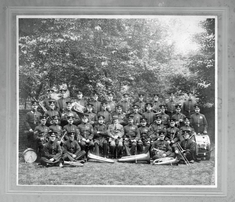 METROPOLITAN POLICE BAND 'J' DIVISION (HACKNEY)
The bandsmen are wearing a cap badge as illustrated in 'Helmets & Cap Badges' #01372.
The officer to the right of the civilian is wearing a cap badge of the 1910-1936 pattern (01364)
As there are a lot of 1911 Coronation medals worn and no WW1 military I would presume it was taken shortly after the Coronation.
