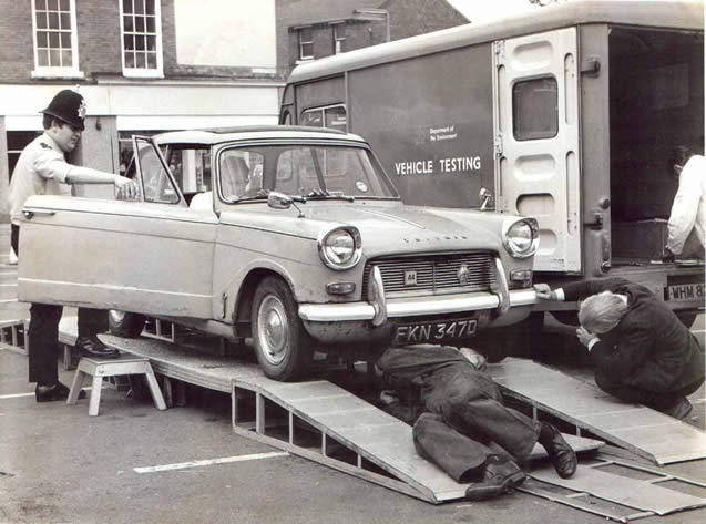 Ministry Roadside Inspections
1975 Hucknall Market Place, Nottinghamshire, and PC 46 David Anson tries to look interested for the local press who, desperate for a story, descended on the Ministry-men scrutinising a Triumph Herald.  Required to stop vehicles selected by the civvy examiners and to report any offences disclosed, this was never one of the most popular of jobs.
Keywords: Hucknall Nottinghamshire